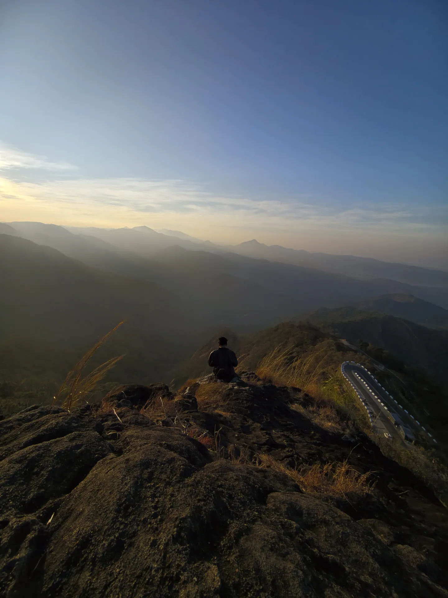 A dark mountain ridge running to the horizon at sunrise, with one small figure sitting on the highest rock.